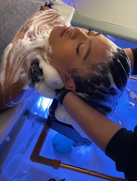 Milbon shampoo lather being worked through a guest's hair at the head spa basin